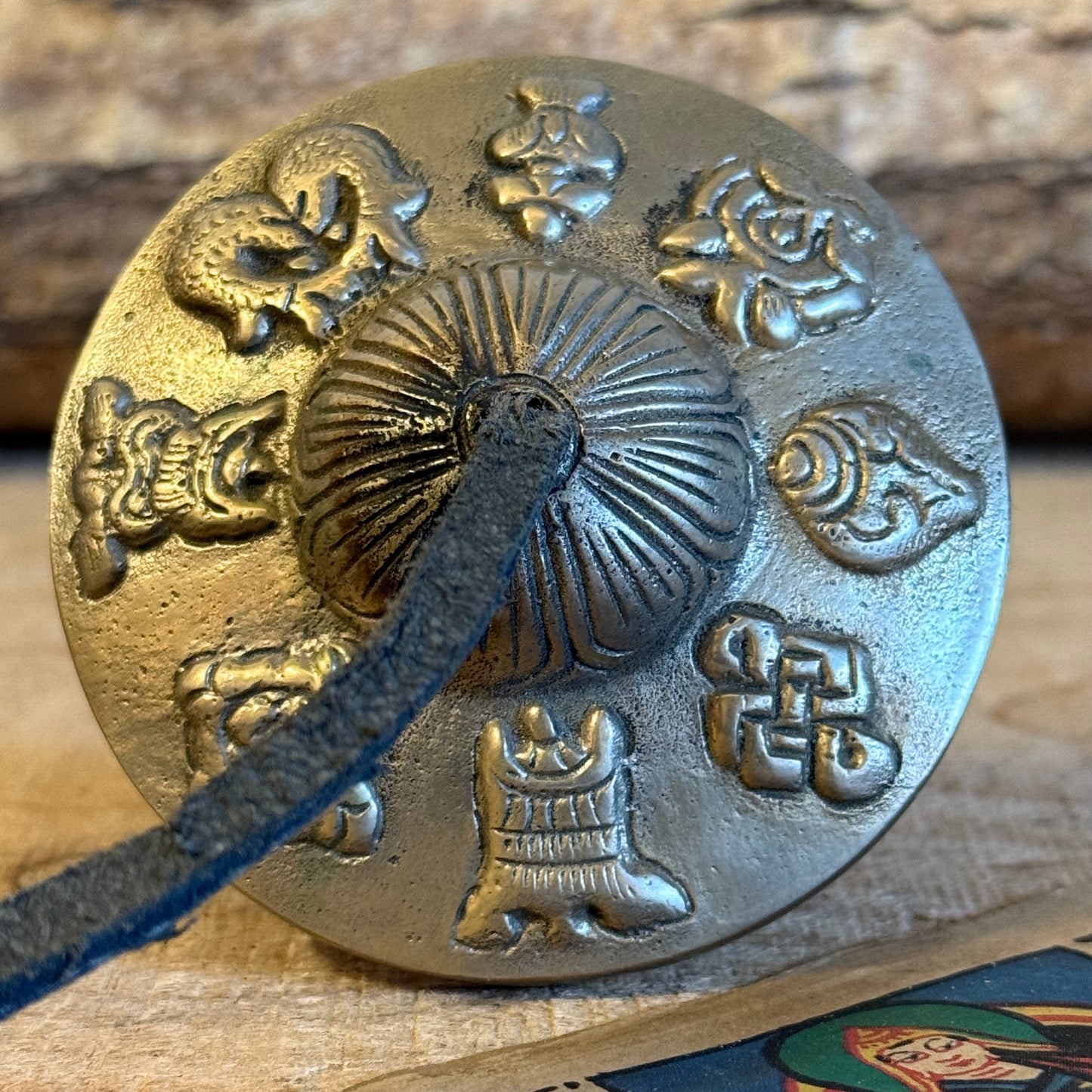 A Tingsha is a small pair of hand-cymbals traditionally used in Tibetan Buddhist practices. They consist of two small, round metal plates connected by a leather or fabric strap. When struck together, they produce a clear, high-pitched, and resonant tone.
