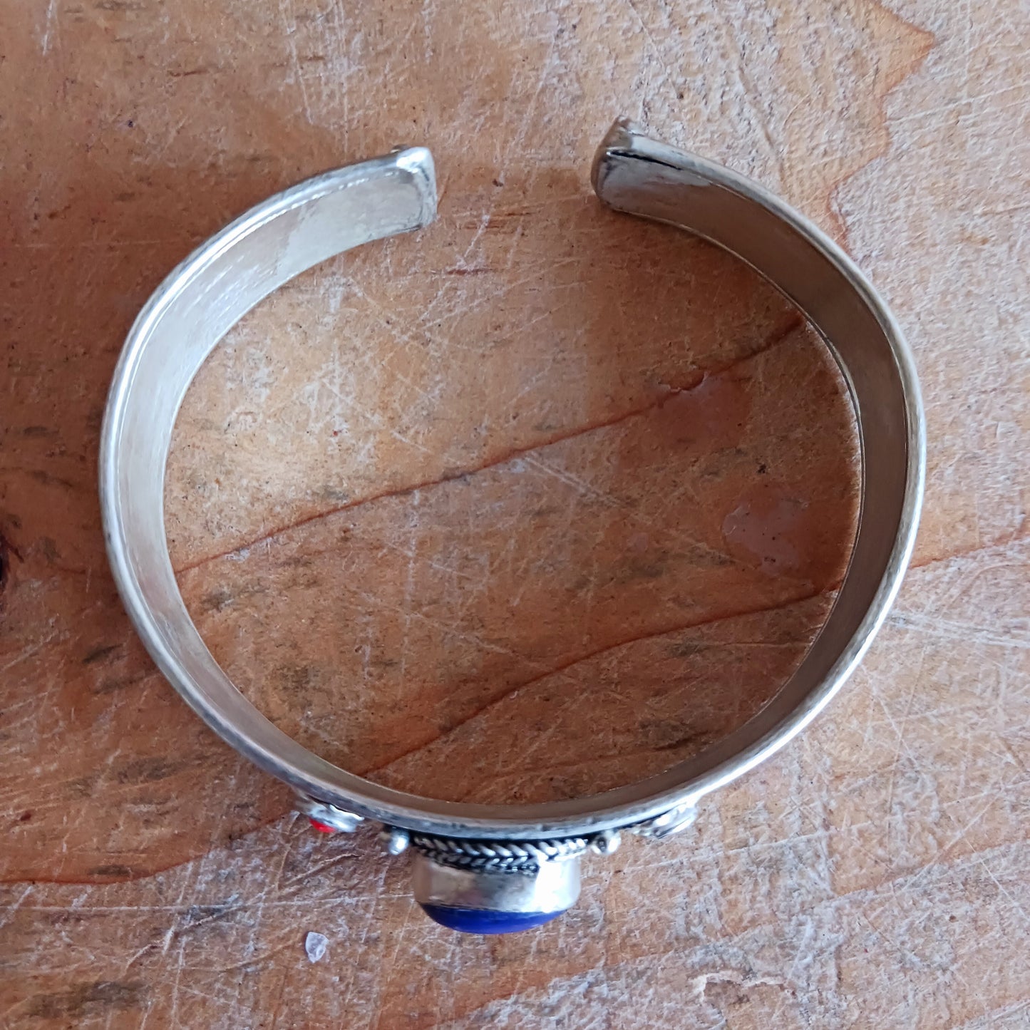 Add a touch of elegance and meaning to your jewellery collection with this handcrafted Nepalese bangle. Made from high-quality white metal, each bangle features a single Lapis stone, flanked by two vibrant red drop beads for a striking contrast.