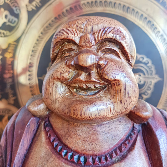 This charming Hand Carved Laughing Buddha is seated in a relaxed pose with a broad, joyful grin and rounded belly, beautifully carved from warm two-tone wood. The natural wood grain is enhanced with a protective varnish, highlighting the intricate details of his robes, prayer beads and expressive face.