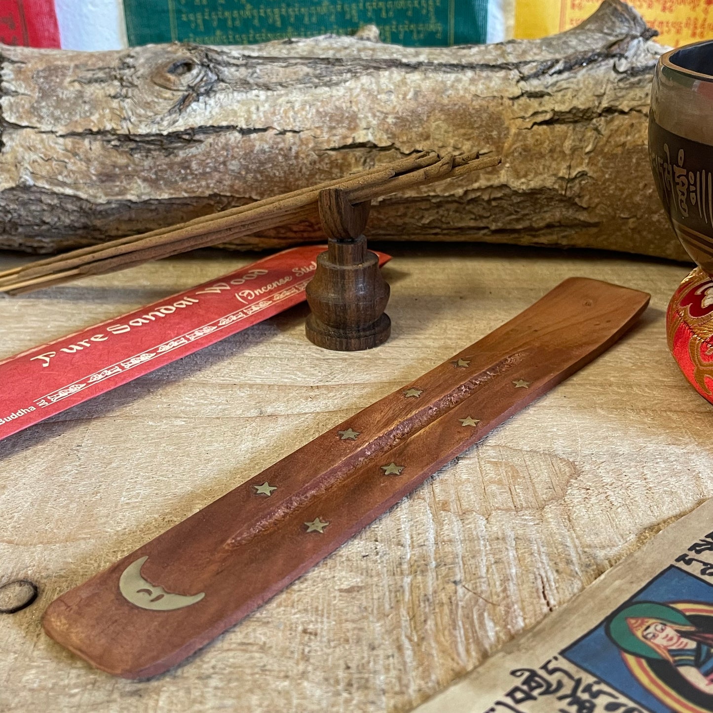 This wooden incense holder is a beautiful ash catcher with a celestial design, ideal for enhancing the atmosphere of any space. Crafted from natural wood and inlaid with a brass moon and stars pattern, this piece is both functional and decorative. Its slightly curved design holds stick incense securely while catching falling ash, keeping your surroundings clean.