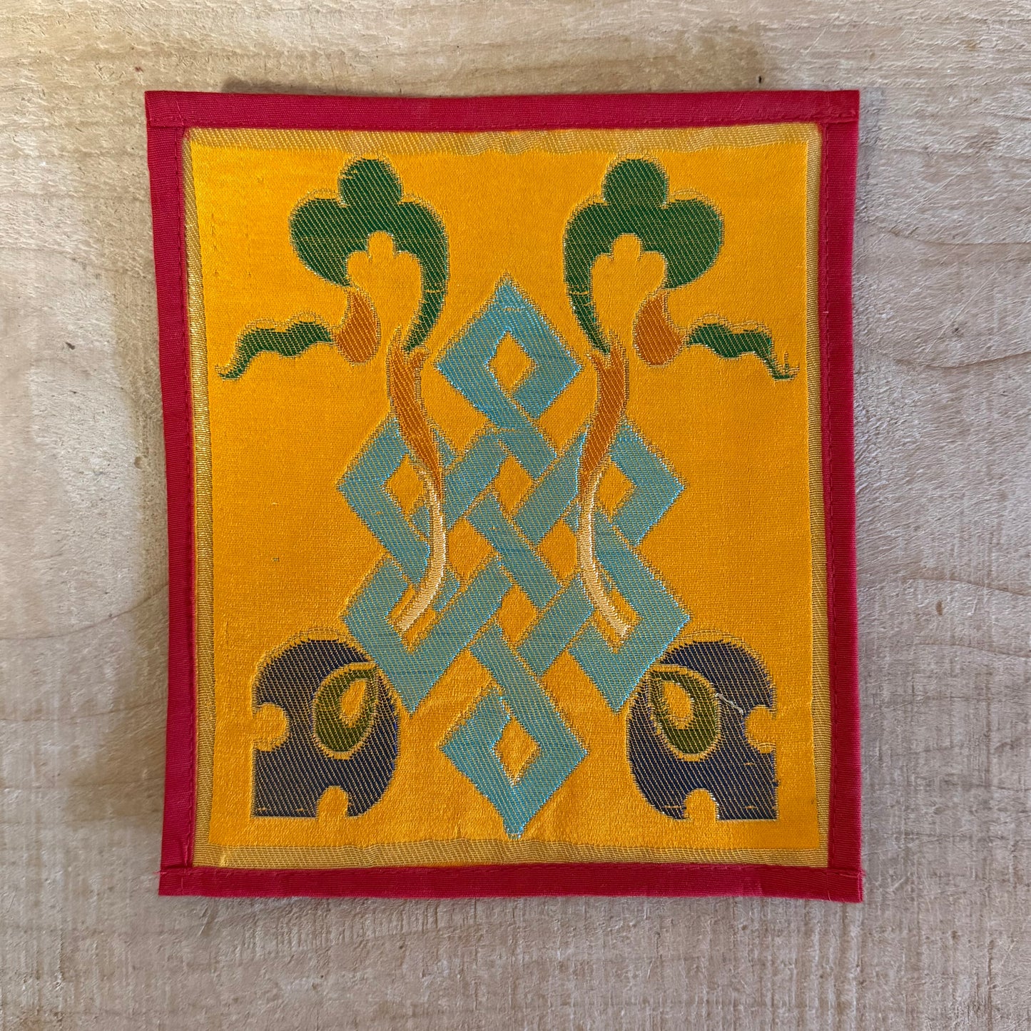 This Mini Tibetan altar cloth features a Dorje and an Endless Knot, symbolizing love, compassion, and the interconnectedness of all things. Handcrafted from thick silk brocade, this silk brocade altar mat is ideal for placement under a singing bowl, standing Dorje, or other sacred Buddhist ornaments.