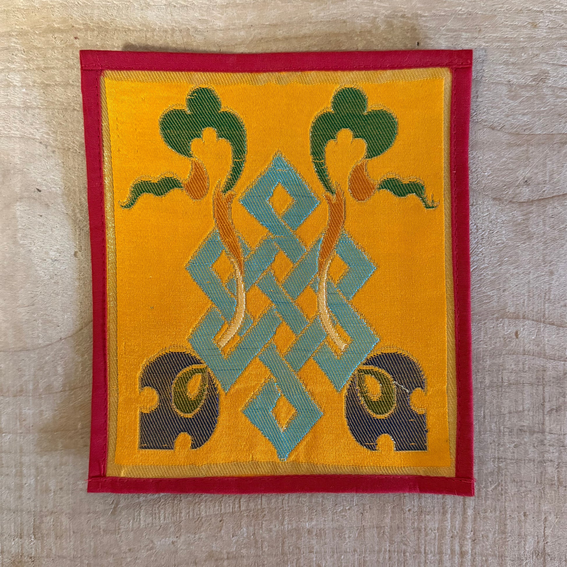 This Mini Tibetan altar cloth features a Dorje and an Endless Knot, symbolizing love, compassion, and the interconnectedness of all things. Handcrafted from thick silk brocade, this silk brocade altar mat is ideal for placement under a singing bowl, standing Dorje, or other sacred Buddhist ornaments.