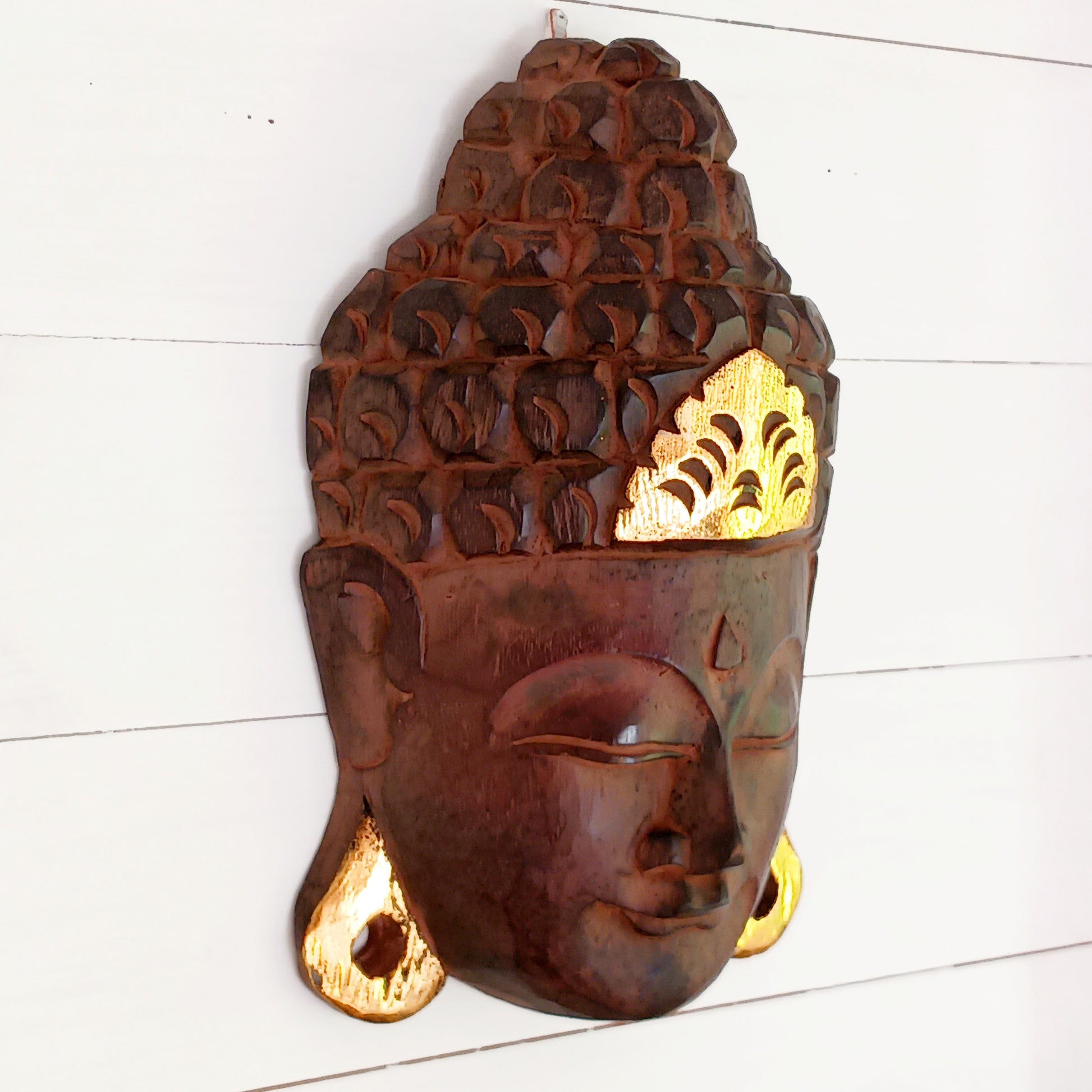 This skillfully crafted wall art of Lord Buddha with its beautiful, serene expression is both rustic and well-polished,  This mask has been hand carved from rain-tree wood by Indonesian artisans and is finished with gold leaf effect embellishment.&nbsp;  As this item is hand carved slight variations should be expected.  Size: Approx: 19cm × 28cm × 9cm Handmade and Fairtrade from Indonesia