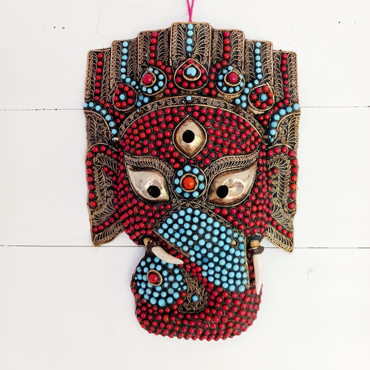 This stunning vintage handmade Lord Ganesh wearable mask | wall decor has multi stone embellishment detail. The colourful mask has hundreds of coral and turquoise stones set into brass wire-scrolls in the cloisonne manner. The third eye of insight is central to the mask. The piece is finished with beautiful, handcrafted filigree.