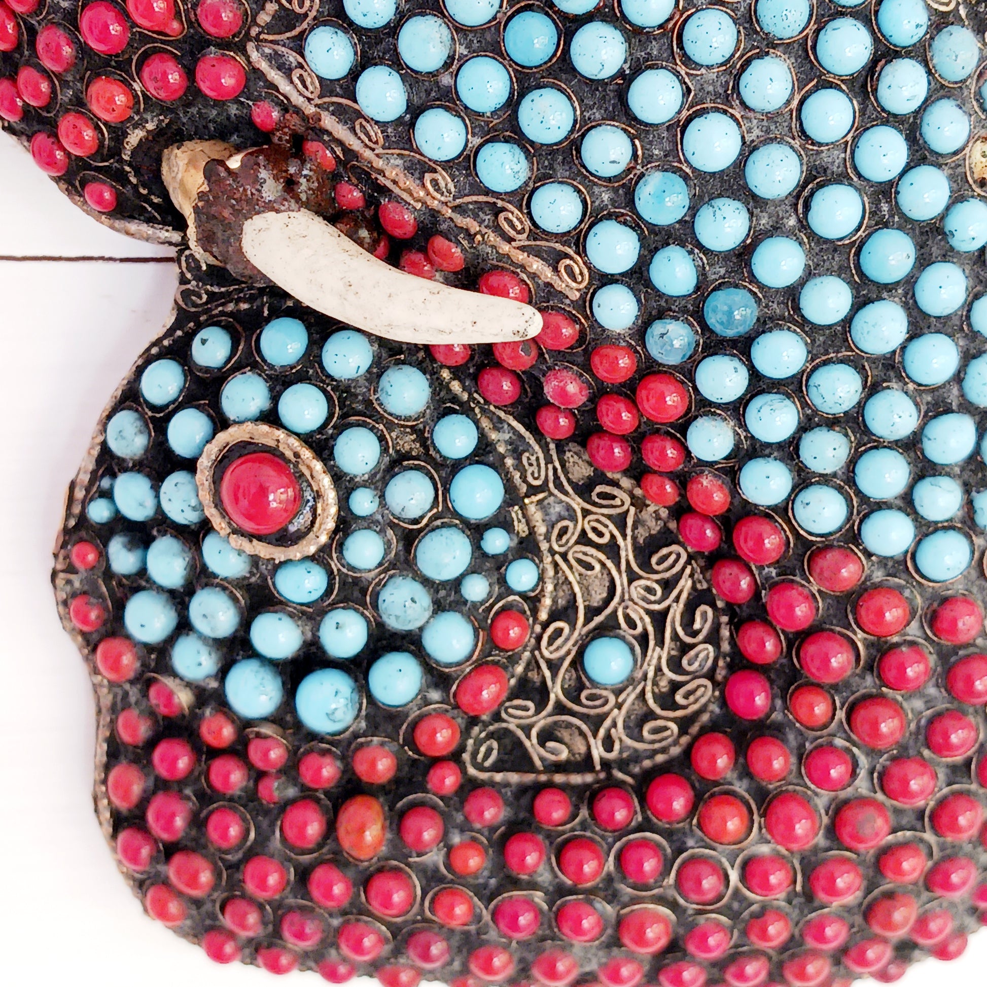 This stunning vintage handmade Lord Ganesh wearable mask | wall decor has multi stone embellishment detail. The colourful mask has hundreds of coral and turquoise stones set into brass wire-scrolls in the cloisonne manner. The third eye of insight is central to the mask. The piece is finished with beautiful, handcrafted filigree.