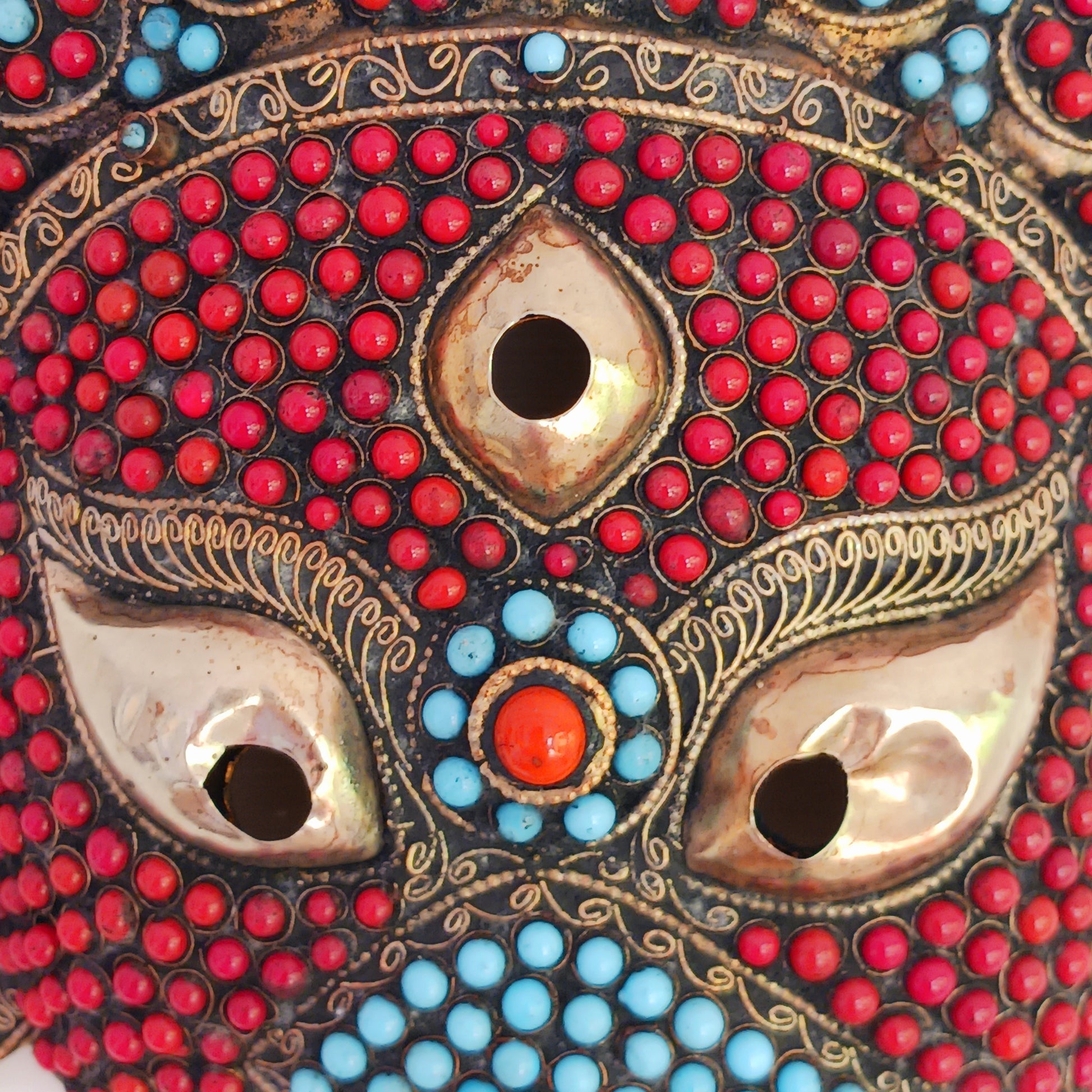 This stunning vintage handmade Lord Ganesh wearable mask | wall decor has multi stone embellishment detail. The colourful mask has hundreds of coral and turquoise stones set into brass wire-scrolls in the cloisonne manner. The third eye of insight is central to the mask. The piece is finished with beautiful, handcrafted filigree.