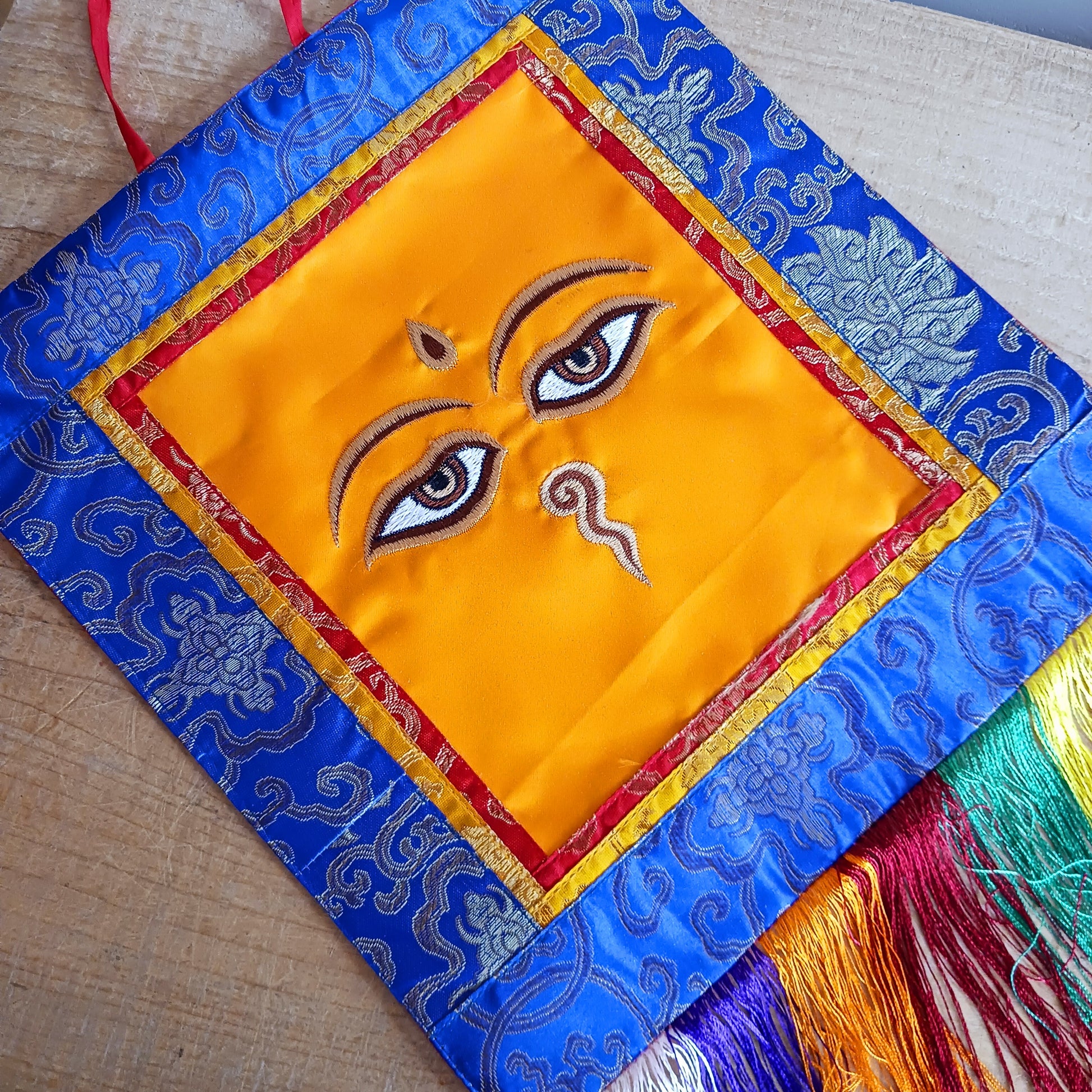 Representing an all-seeing, omniscient Buddha, these embroidered banners depict two eyes in the four cardinal directions, and the Nepali character for the number 1 sits between them like a question mark. This symbolizes the unity of all things and the one path to enlightenment.