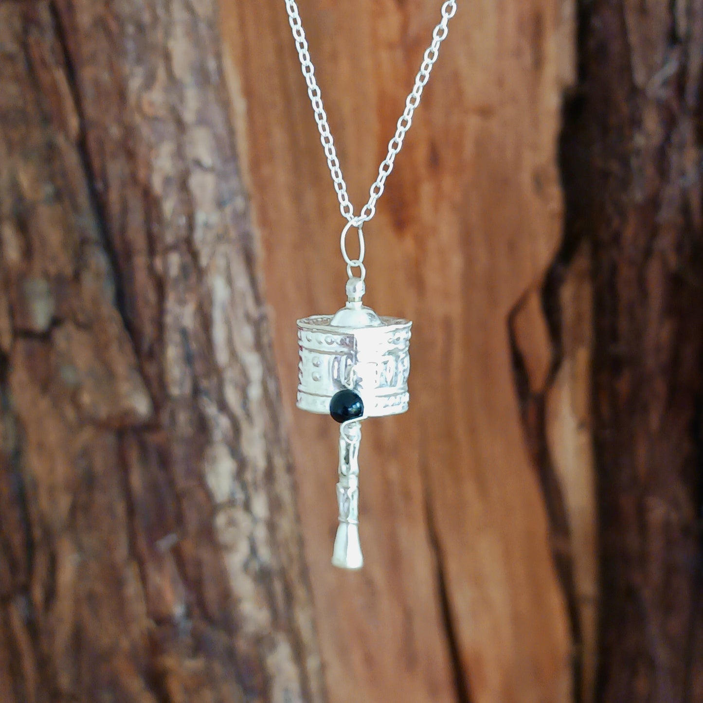 This Tibetan silver prayer wheel pendant has a Tibetan mantra engraved around the wheel.