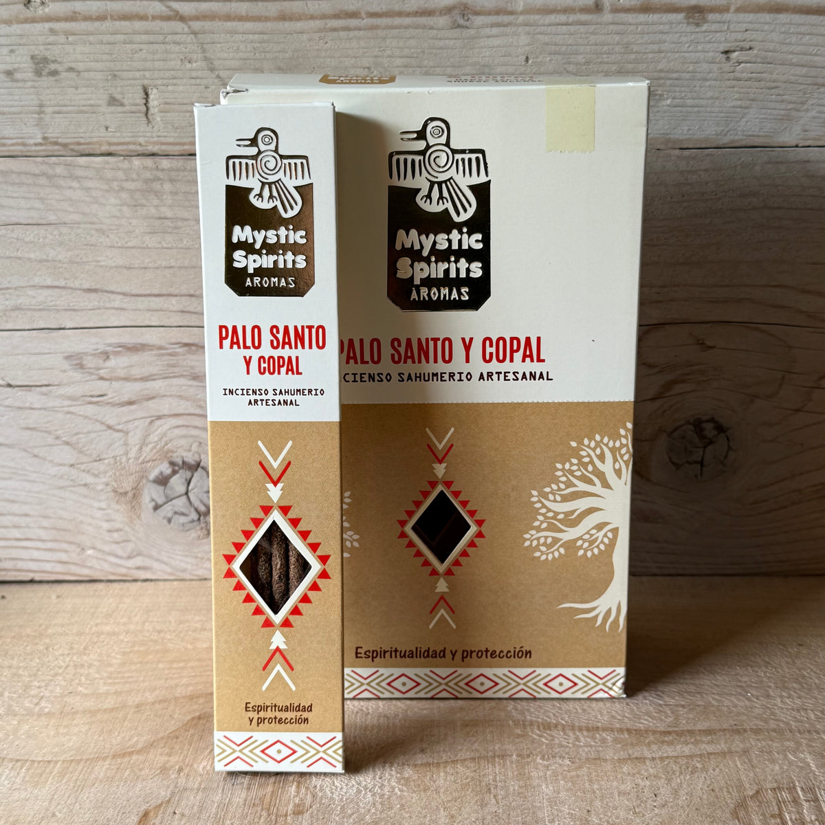 Two boxes of Mystic Spirits Aromas Palo Santo and Copal incense sticks standing upright on a light wood surface against a rustic wood plank background.