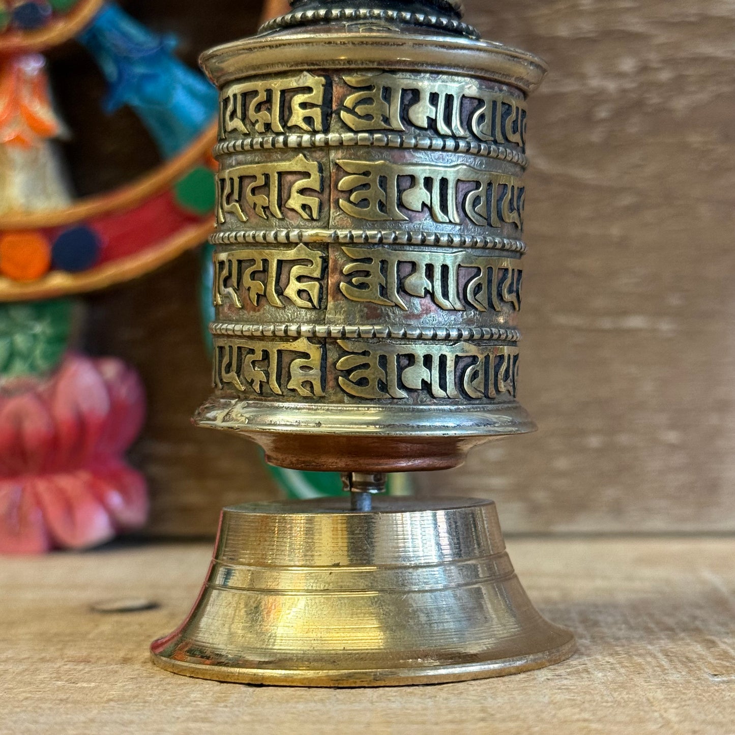 This Mini Tabletop Prayer Wheel is a sacred object of quiet power and devotion. Though small in size, it contains great merit—filled with countless scrolls of the Om Mani Padme Hum mantra, the heart-essence of compassion.

Crafted from a mix of copper and solid brass, the wheel features four lines of sacred mantra around its exterior and rests on a finely detailed brass base. According to Tibetan Buddhist tradition, spinning the prayer wheel is equal in merit to reciting the mantra aloud, purifying negativi