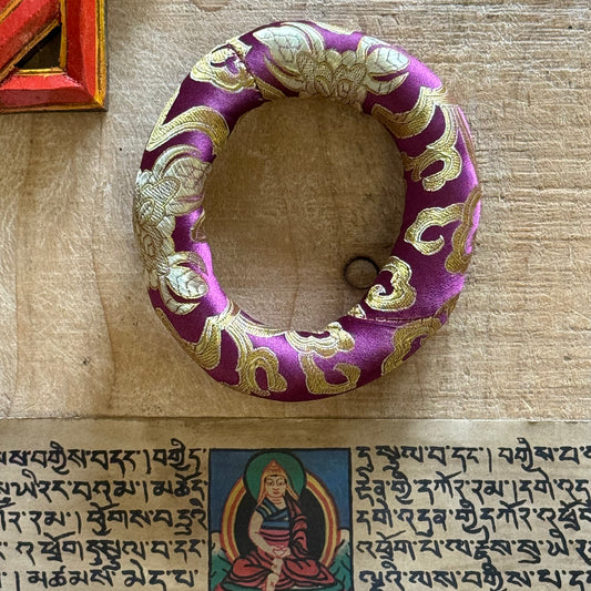 Cradle your singing bowl in divine comfort with our 11cm Doughnut Singing Bowl Cushion. As a practitioner of sound healing, I understand how every detail matters in sacred practice—including how your instruments rest when not in use.

This luxurious brocade ring isn't just a cushion; it's a ceremonial throne for your singing bowl. Designed to support smaller to medium-sized bowls, its doughnut shape stabilizes your bowl gently, allowing it to radiate its pure tones without interference. Whether you're medit