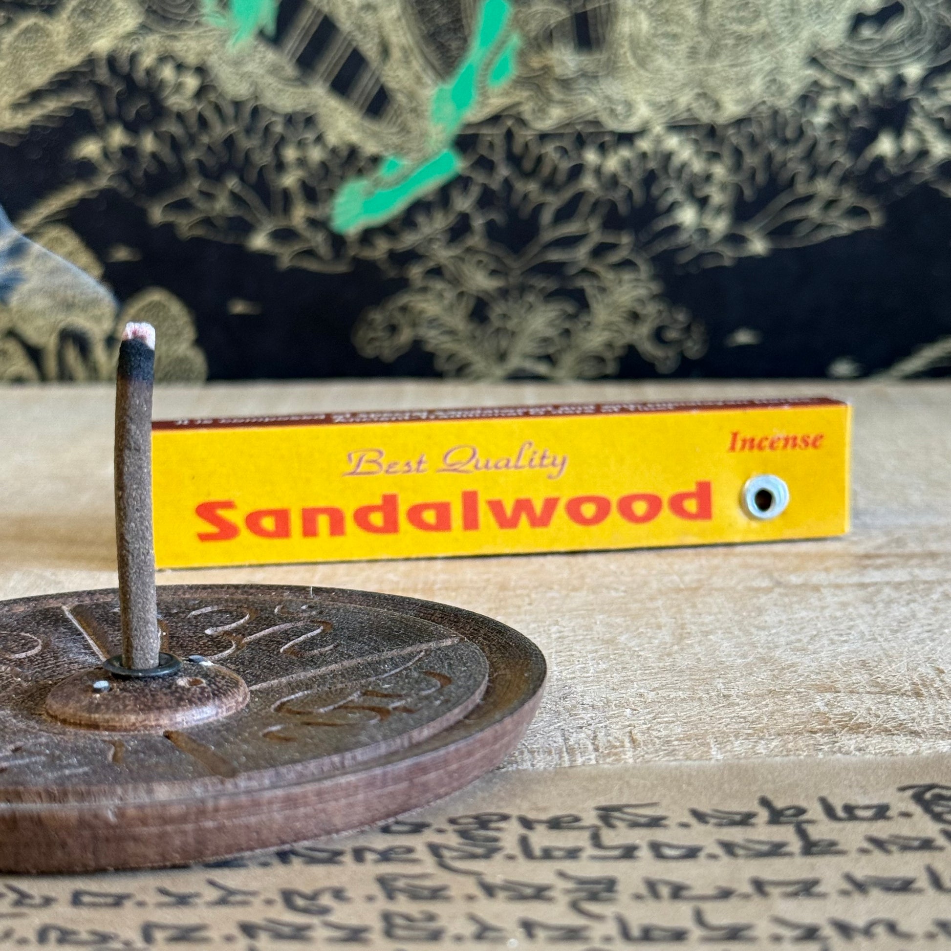 Sandalwood incense stick and box on a textured surface with a decorative background