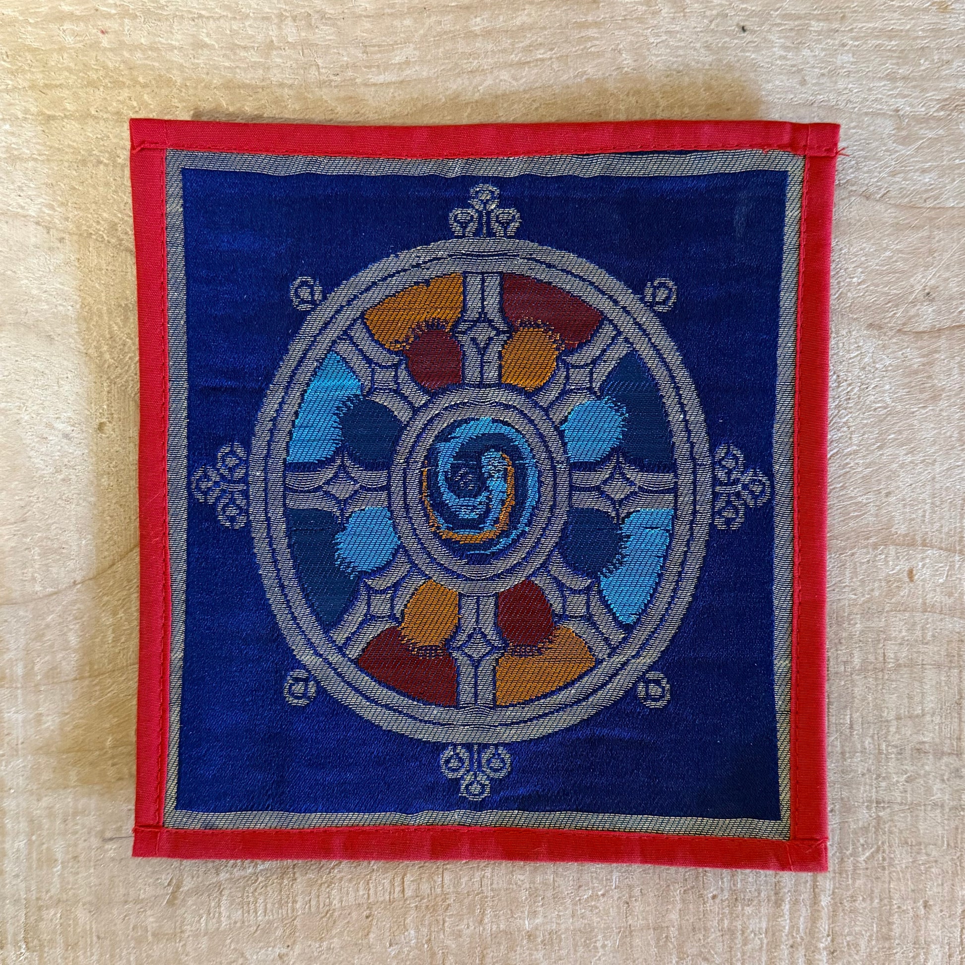 This Mini Tibetan altar cloth features a Dorje (Vajra) and a Dharma Wheel, representing the indestructible power of love, compassion, and spiritual protection. Handcrafted from thick silk brocade, this silk brocade altar mat is ideal for placement under a singing bowl, standing Dorje, or other sacred Buddhist ornaments.