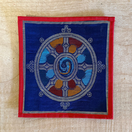 This Mini Tibetan altar cloth features a Dorje (Vajra) and a Dharma Wheel, representing the indestructible power of love, compassion, and spiritual protection. Handcrafted from thick silk brocade, this silk brocade altar mat is ideal for placement under a singing bowl, standing Dorje, or other sacred Buddhist ornaments.