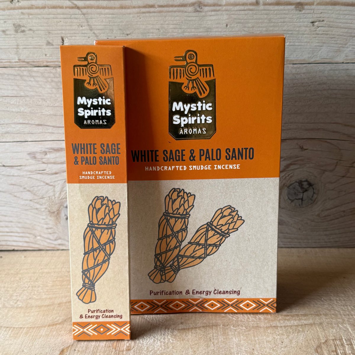Two boxes of Mystic Spirits Aromas White Sage & Palo Santo handcrafted snudge incense standing upright on a light wood surface against a rustic wood plank background.