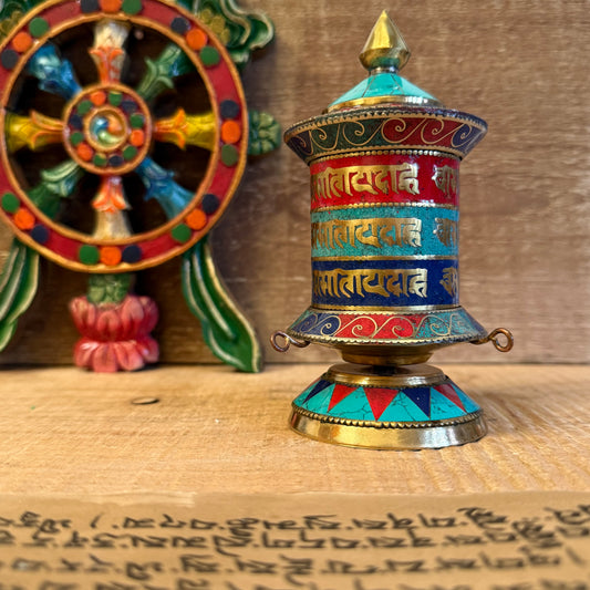 In the quiet turning of this prayer wheel, the sacred syllables of compassion and wisdom are whispered into the world. Handcrafted from copper and brass, this 14cm desktop prayer wheel contains a scroll inscribed with countless repetitions of the sacred Om Mani Padme Hum mantra.

Each gentle spin of the wheel is a spiritual act—an offering of peace, merit, and mindfulness. Adorned with stone chips and the timeless Om symbol, it serves not only as a meditation aid but also as a humble ornament of devotion fo