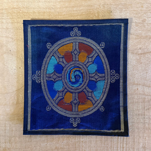 This Mini Tibetan altar cloth features a Dorje and a bold Dharma Wheel, symbolizing love, compassion, and spiritual protection. Handcrafted from thick silk brocade, this silk brocade altar mat is perfect for placement under a singing bowl, standing Dorje, or other sacred Buddhist ornaments.