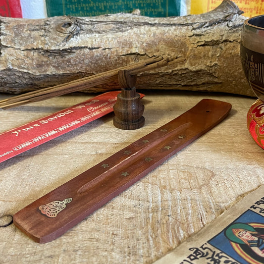 This wooden incense holder is thoughtfully designed as a practical and spiritual ash catcher. Adorned with brass inlays featuring a serene Buddha and stars motif, it adds a sense of peace and calm to your incense rituals. The holder's wooden body gently curves to cradle incense sticks securely, allowing ash to fall neatly onto the base to keep your surfaces clean.