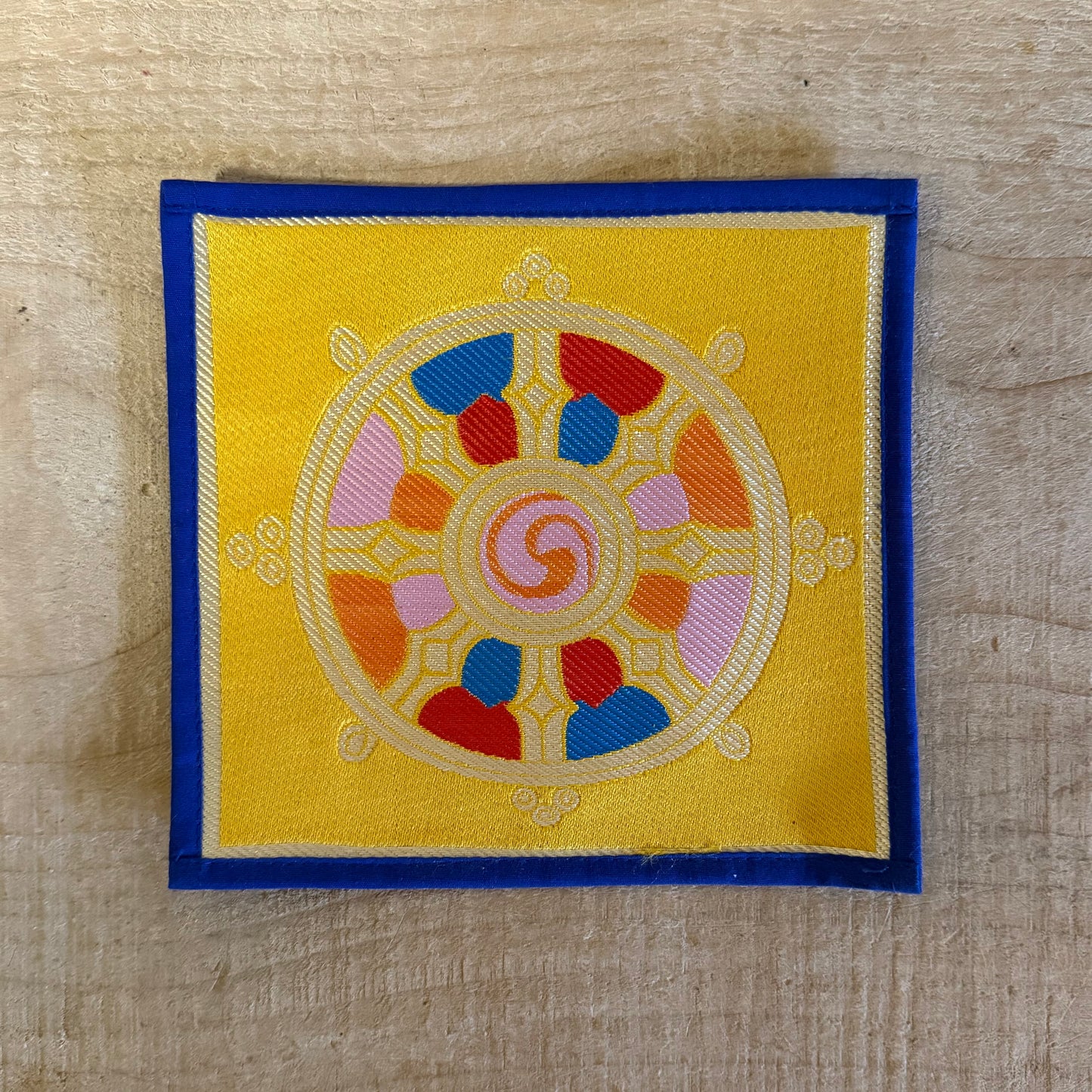 This Mini Tibetan altar cloth features a Dorje and a bold Dharma Wheel, symbols of love, compassion, and spiritual protection. Handcrafted from thick silk brocade, this silk brocade altar mat is ideal for placement under a singing bowl, standing Dorje, or other sacred Buddhist ornaments.