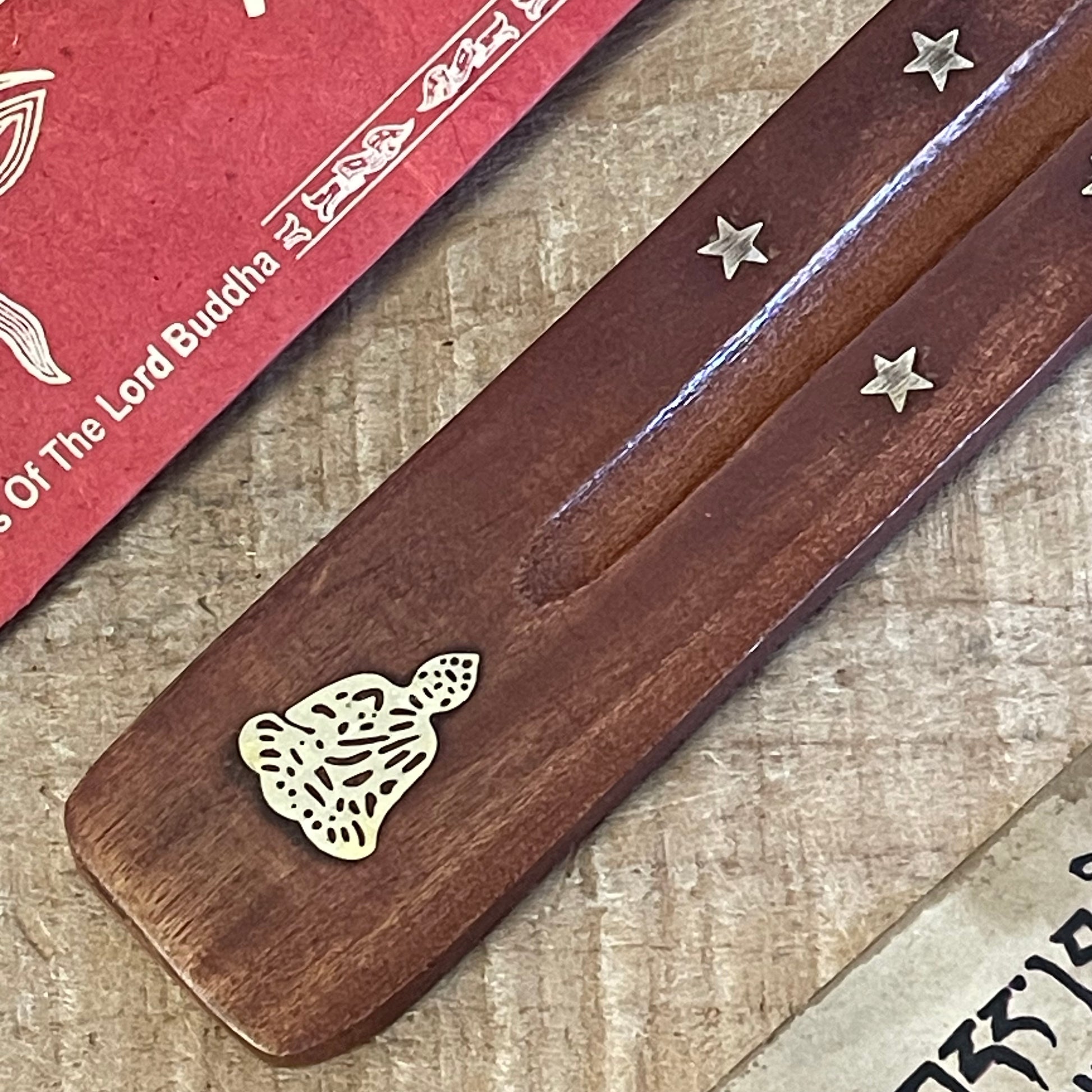 This wooden incense holder is thoughtfully designed as a practical and spiritual ash catcher. Adorned with brass inlays featuring a serene Buddha and stars motif, it adds a sense of peace and calm to your incense rituals. The holder's wooden body gently curves to cradle incense sticks securely, allowing ash to fall neatly onto the base to keep your surfaces clean.