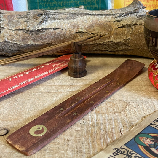 This wooden incense holder serves as a graceful ash catcher with a symbolic touch, featuring a brass inlay design of the Yin Yang and stars. Representing harmony and balance, the Yin Yang symbol adds a calming energy to your space, perfect for meditation or relaxation. The slightly curved wooden body securely holds incense sticks, allowing ash to fall neatly onto the base for easy cleanup.

Features:
Material: Wood with brass inlay
Design: Yin Yang and stars brass inlay pattern
Dimensions: Approximately 3 c