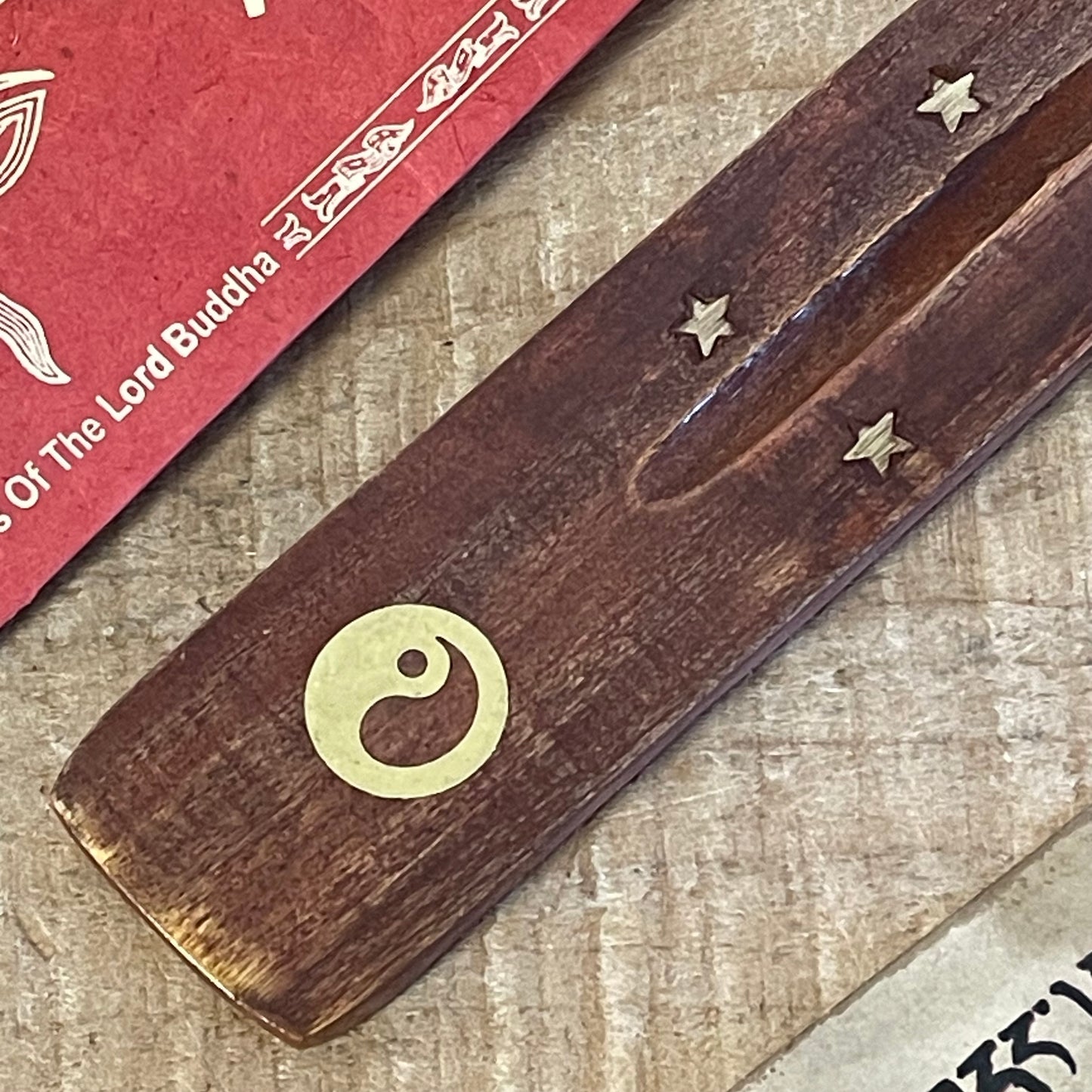 This wooden incense holder serves as a graceful ash catcher with a symbolic touch, featuring a brass inlay design of the Yin Yang and stars. Representing harmony and balance, the Yin Yang symbol adds a calming energy to your space, perfect for meditation or relaxation. The slightly curved wooden body securely holds incense sticks, allowing ash to fall neatly onto the base for easy cleanup.

Features:
Material: Wood with brass inlay
Design: Yin Yang and stars brass inlay pattern
Dimensions: Approximately 3 c