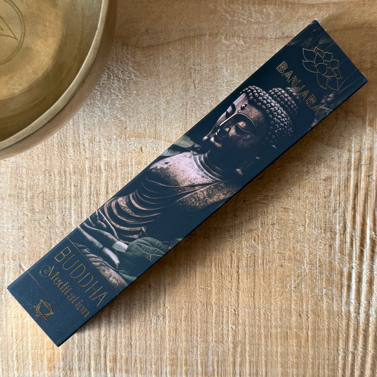 A long rectangular box of Buddha Meditation incense sticks by BANARA, featuring a dark blue design with a Buddha statue image and gold lettering, placed diagonally on a light wood surface.