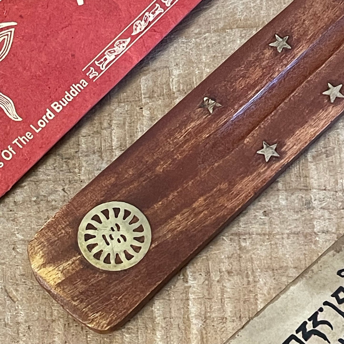 This wooden incense holder is designed as a simple, effective ash catcher with a classic, earthy aesthetic. Crafted from wood and adorned with brass inlays featuring a sun and stars motif, this design brings a touch of celestial charm to your incense rituals. The wooden body is slightly curved to hold incense sticks securely, while allowing ash to fall cleanly onto the base, keeping surfaces tidy.