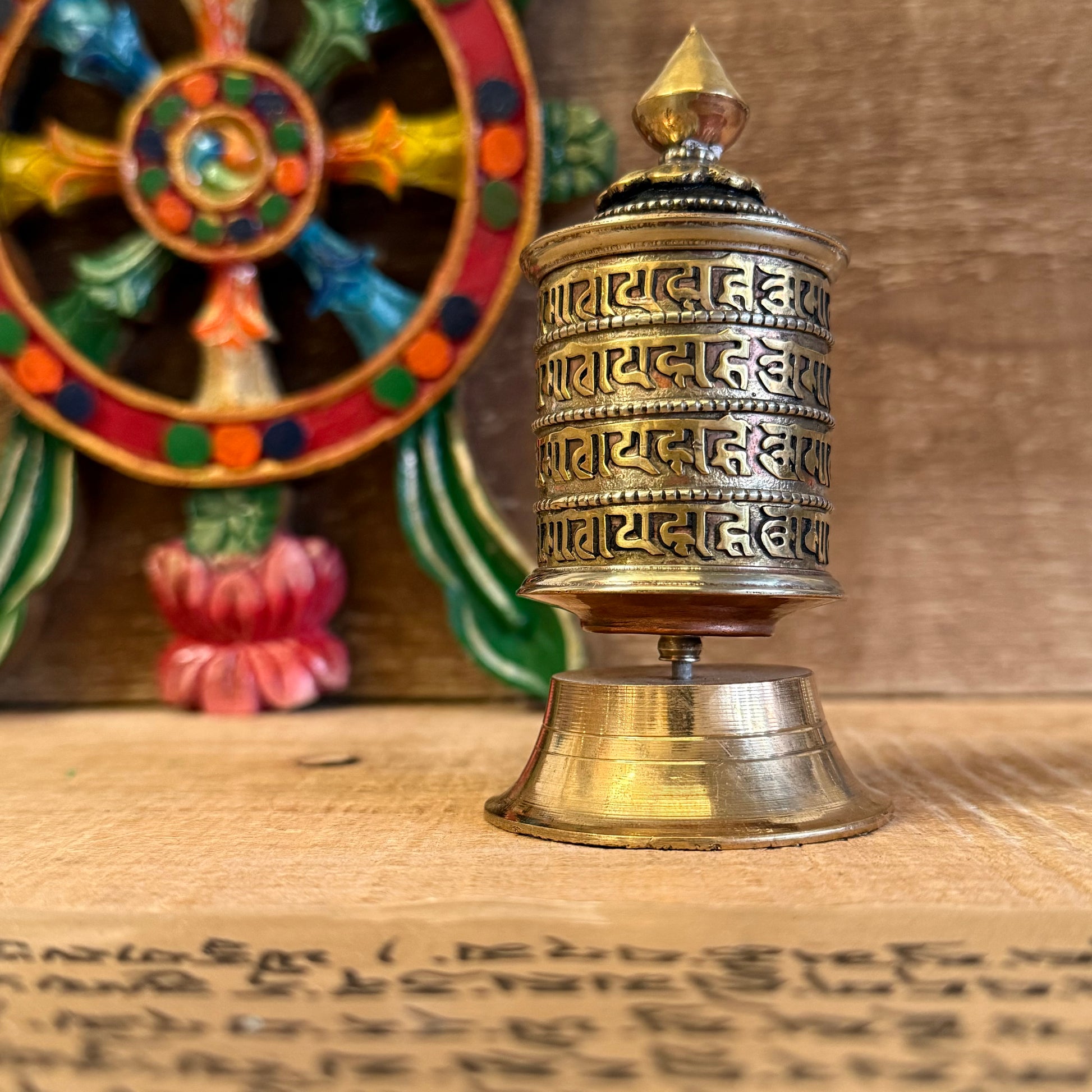 This Mini Tabletop Prayer Wheel is a sacred object of quiet power and devotion. Though small in size, it contains great merit—filled with countless scrolls of the Om Mani Padme Hum mantra, the heart-essence of compassion.

Crafted from a mix of copper and solid brass, the wheel features four lines of sacred mantra around its exterior and rests on a finely detailed brass base. According to Tibetan Buddhist tradition, spinning the prayer wheel is equal in merit to reciting the mantra aloud, purifying negativi