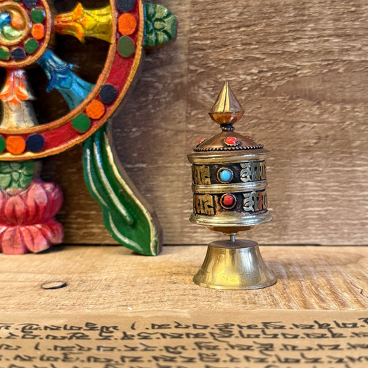Though small in size, this sacred prayer wheel carries the boundless power of the Om Mani Padme Hum mantra.

Handcrafted from a copper and brass mix, this 9cm tabletop prayer wheel is detailed with two lines of sacred inscription and rests upon a solid, ornate brass base. Within the rotating chamber lies a scroll containing countless repetitions of the mantra—believed, in the Tibetan tradition, to bring the same spiritual merit as spoken recitation with every spin.

Compact yet spiritually potent, this whee