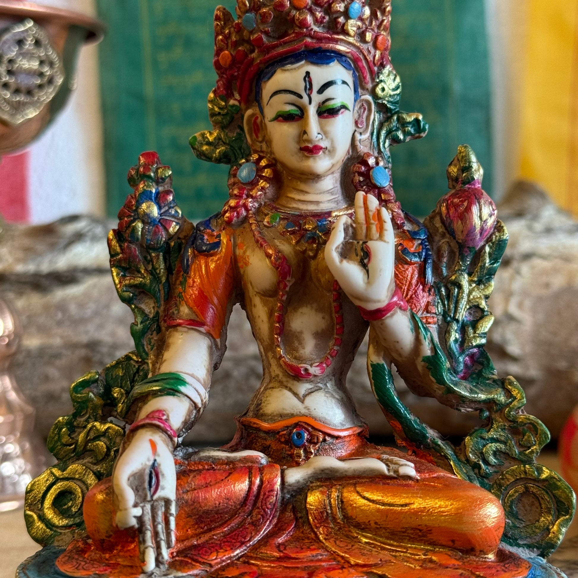 This is a beautifully intricate, handcrafted resin statue depicting White Tara, a revered goddess in Tibetan Buddhism. Known for her embodiment of compassion, healing, serenity, and longevity, she is a symbol of peace and enlightenment. The statue is skillfully painted and highlights White Tara's unique attributes:

Posture: She is seated in a tranquil, full lotus position, which signifies her meditative and composed nature, in contrast to Green Tara's more active pose with one foot extended.
Gesture: Her r