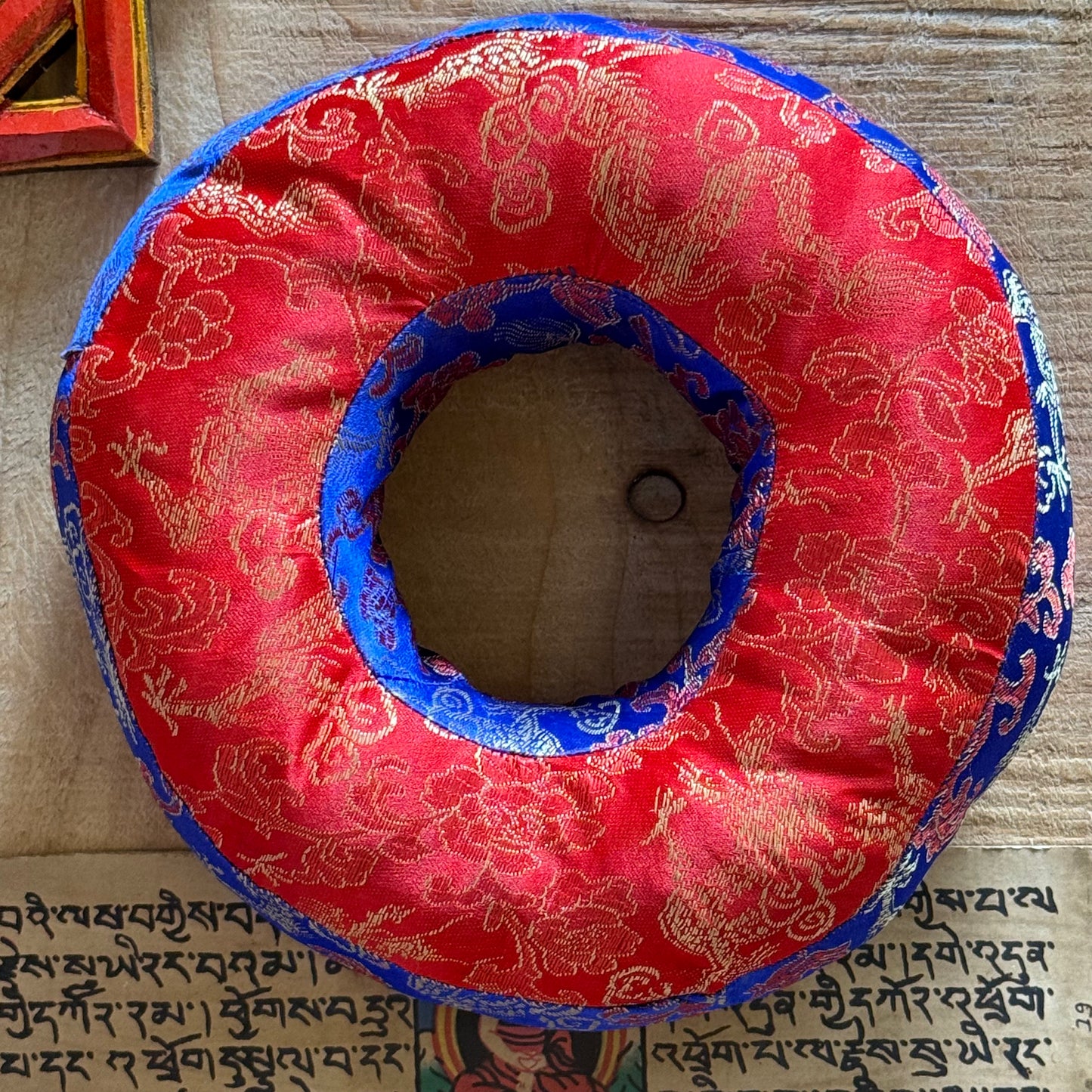 Enhance your meditation practice with this Large Round Donut Singing Bowl Cushion, measuring 18 x 6 cm. Crafted from mixed brocade fabrics, this cushion provides a stable and elegant base for smaller singing bowls, helping to amplify their sound and protect delicate surfaces. Handmade in Nepal under fair trade principles, each cushion reflects traditional craftsmanship and supports local artisans. Its round, stitched design not only complements the bowl’s shape but also adds a touch of serene beauty to your