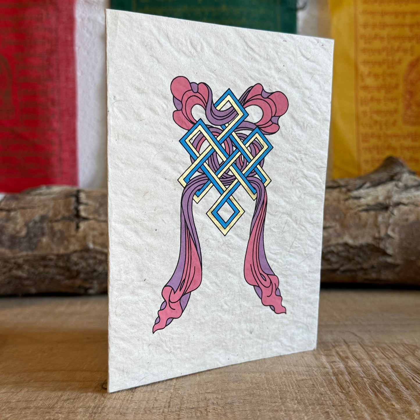 Beautifully coloured and decorated greetings card, made from Lokta paper, featuring the Endless Knot and Treasure Vase.

Lokta paper making is a traditional practice from the high altitude Himalayan forests of Nepal. The Lokta bush is a fast growing shrub and the paper making process helps to provide economic stability for some of Nepal's poorer rural people.

Size: approx. 15.5 x 11.5 cm

☸Buddhist design Lokta paper card with envelopes
☸Made from a sustainable plant source
☸Handmade and Fairtrade from Nep