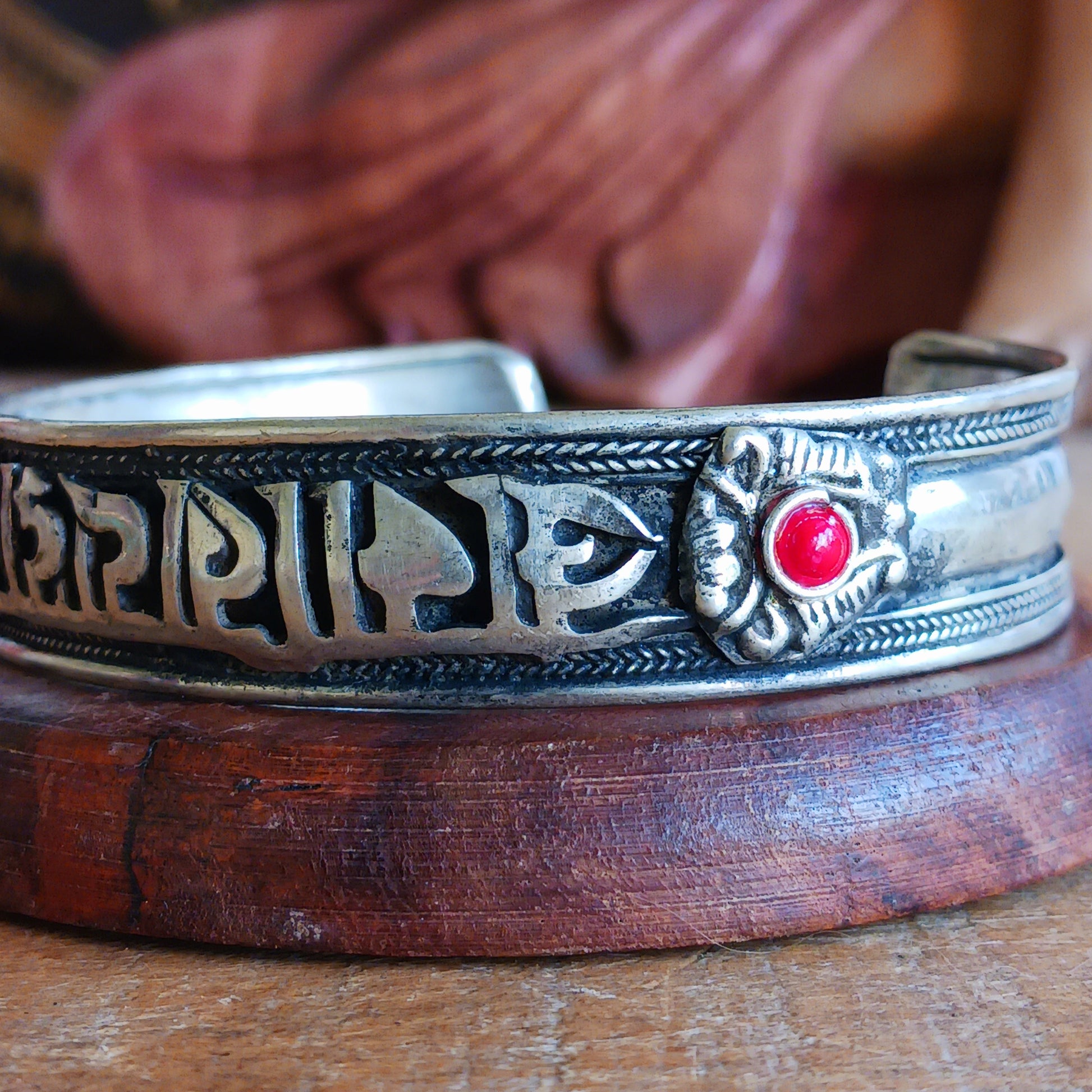 This Tibetan adjustable mantra bangle is a timeless piece of spiritual jewellery, handcrafted by skilled artisans in Nepal. Made from traditional Tibetan White Metal, the bangle features two small coral stones and engraved script inspired by ancient Tibetan culture and symbolism.