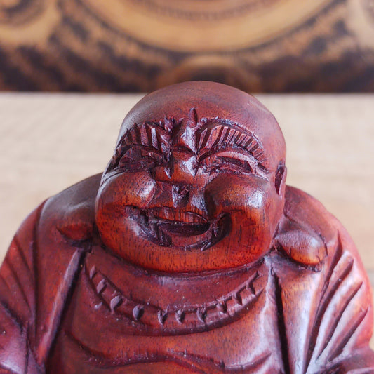 This mini hard carved wooden Laughing Buddha statue represents Budai, the beloved figure of joy, abundance, and contentment in Buddhist tradition. Carved in wood and full of character, Budai is traditionally depicted as a bald monk with a joyful smile, wearing simple robes and holding prayer beads.