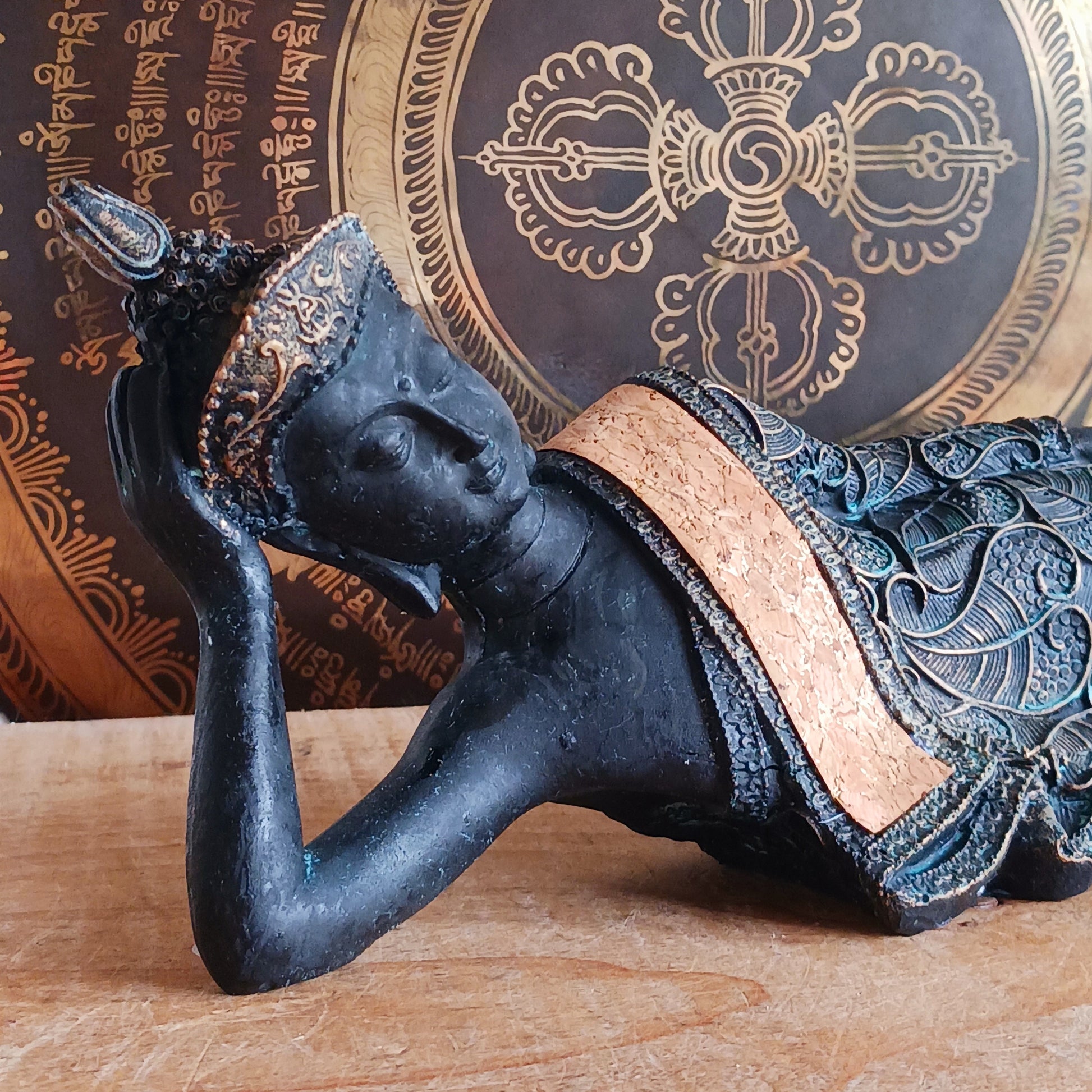 The statue features the Buddha in a graceful reclining pose, symbolizing his entry into nirvana. His left arm rests peacefully by his side, while his right hand cradles his head in a gesture of repose. The robe is intricately adorned with bodhi leaf motifs—sacred symbols of enlightenment and spiritual awakening.