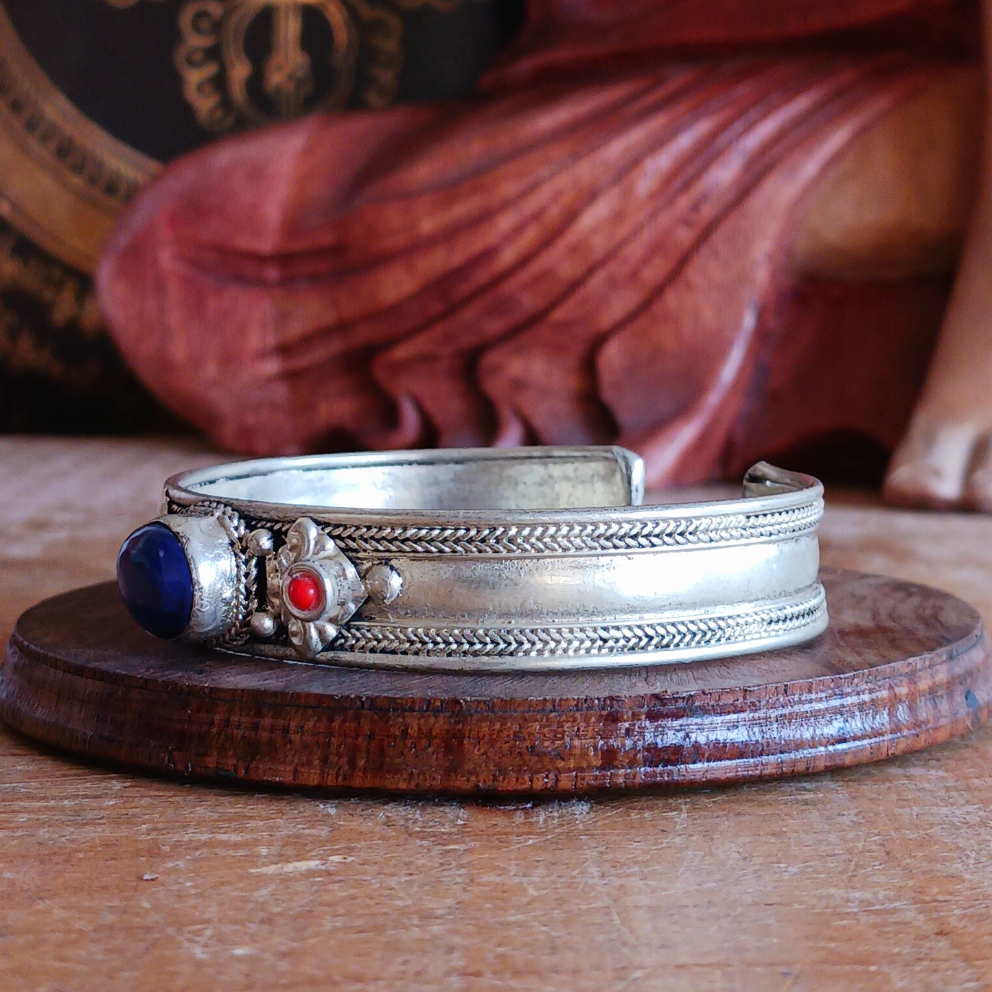 Add a touch of elegance and meaning to your jewellery collection with this handcrafted Nepalese bangle. Made from high-quality white metal, each bangle features a single Lapis stone, flanked by two vibrant red drop beads for a striking contrast.