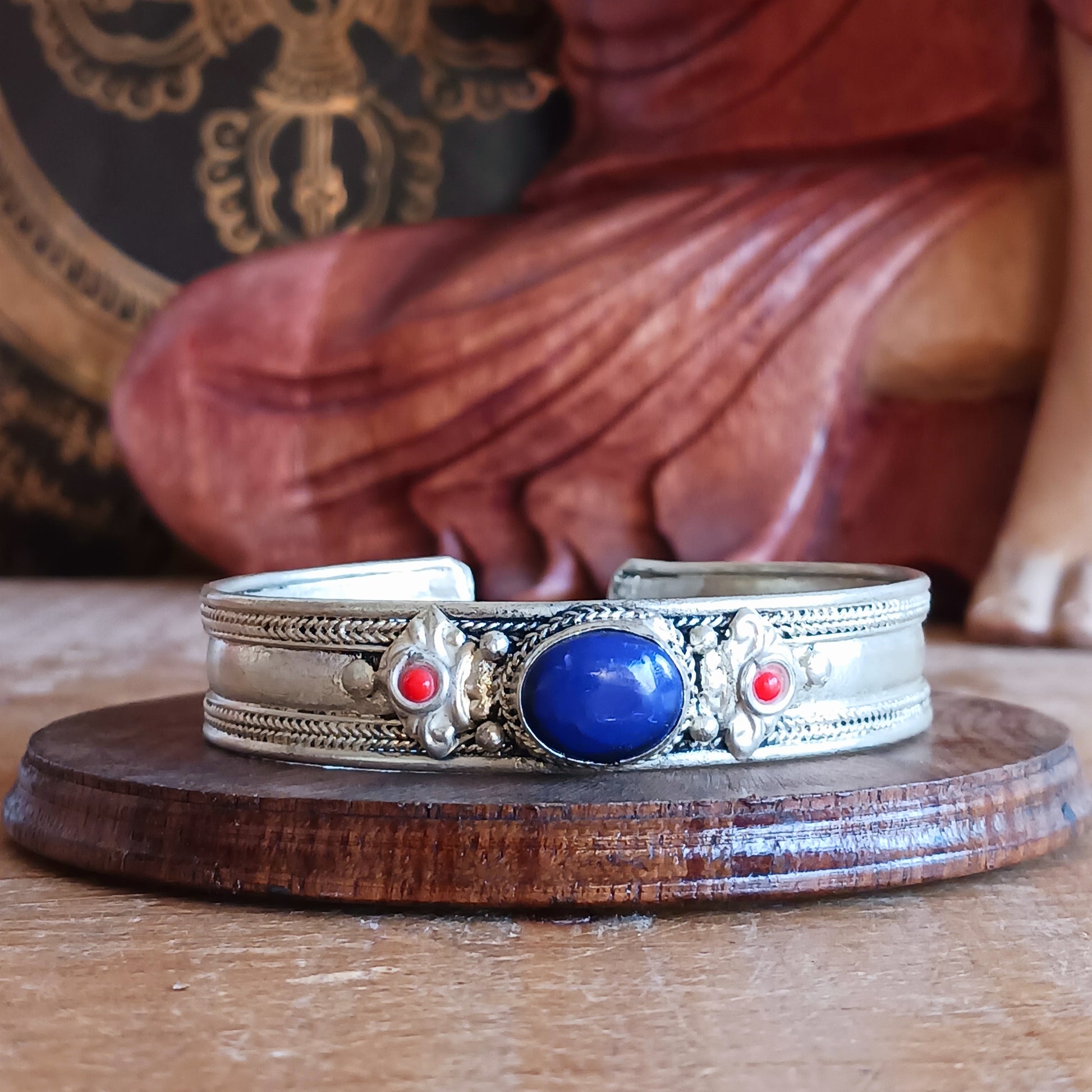 Add a touch of elegance and meaning to your jewellery collection with this handcrafted Nepalese bangle. Made from high-quality white metal, each bangle features a single Lapis stone, flanked by two vibrant red drop beads for a striking contrast.