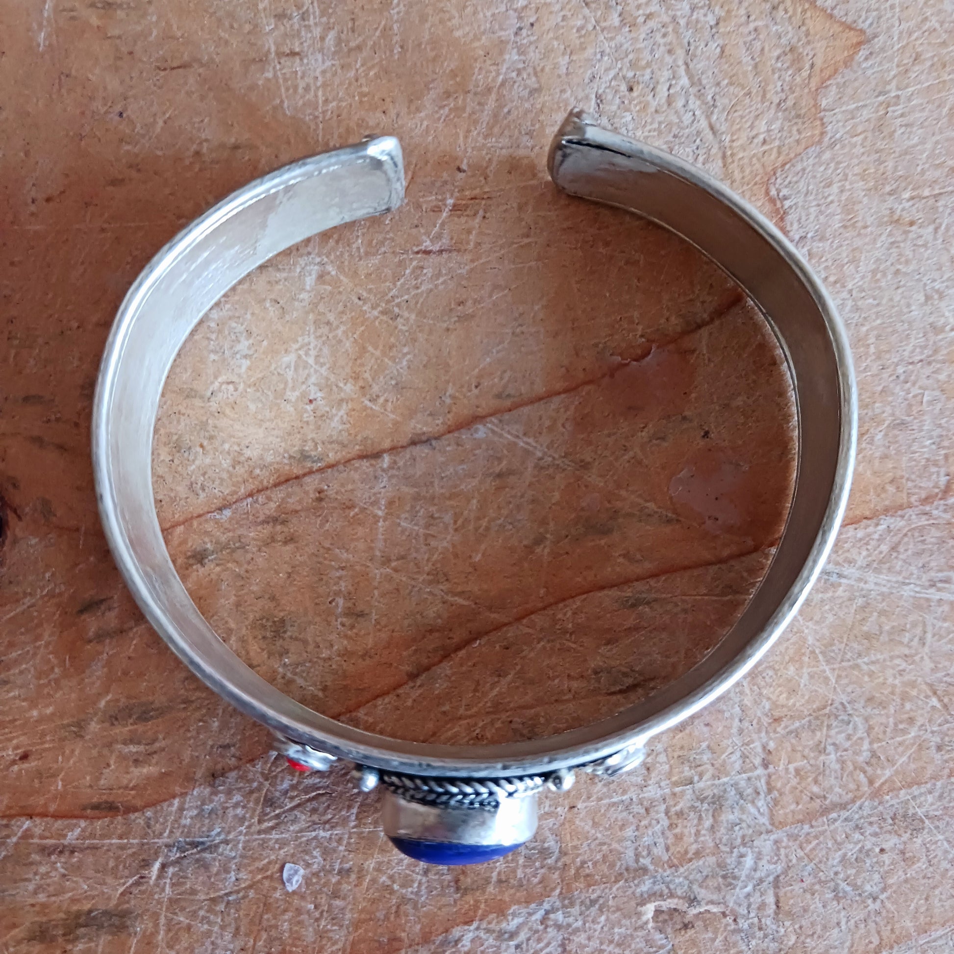 Add a touch of elegance and meaning to your jewellery collection with this handcrafted Nepalese bangle. Made from high-quality white metal, each bangle features a single Lapis stone, flanked by two vibrant red drop beads for a striking contrast.