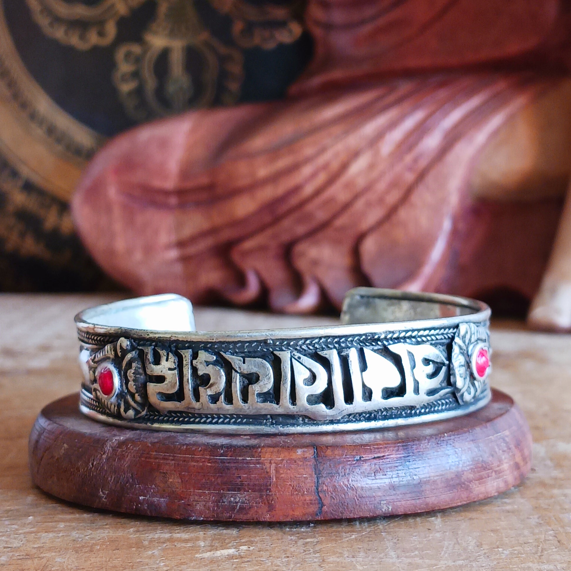 This Tibetan adjustable mantra bangle is a timeless piece of spiritual jewellery, handcrafted by skilled artisans in Nepal. Made from traditional Tibetan White Metal, the bangle features two small coral stones and engraved script inspired by ancient Tibetan culture and symbolism.