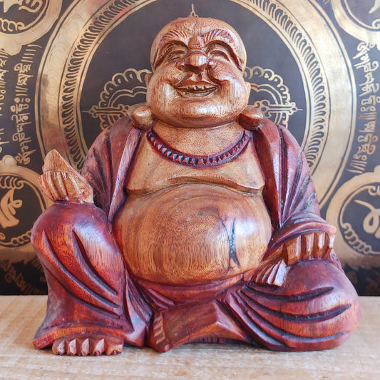 This charming Hand Carved Laughing Buddha is seated in a relaxed pose with a broad, joyful grin and rounded belly, beautifully carved from warm two-tone wood. The natural wood grain is enhanced with a protective varnish, highlighting the intricate details of his robes, prayer beads and expressive face.
