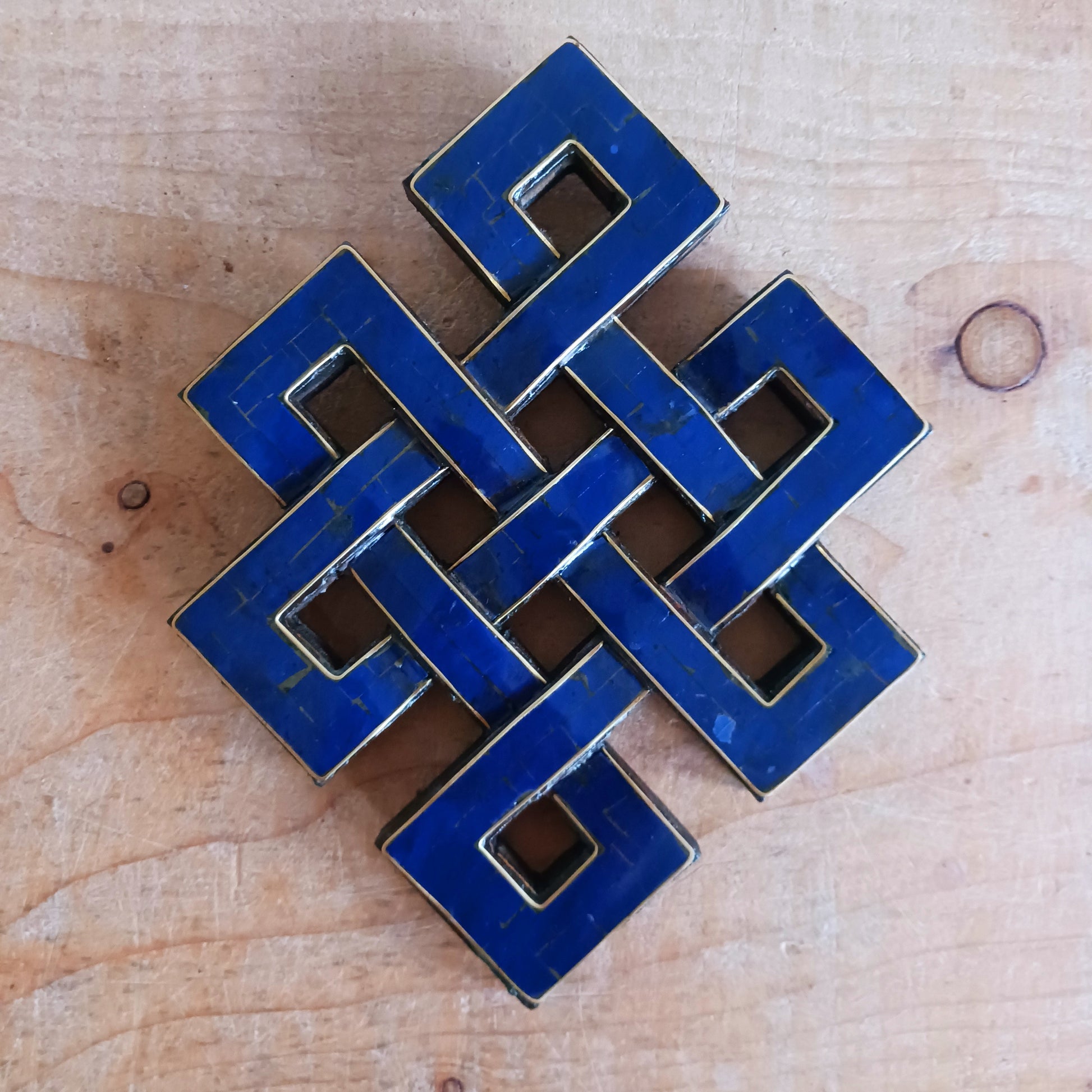 The Eternal (or Endless) Knot is one of the Eight auspicious symbols in Tibetan Buddhism. Because the knot has no beginning and no end, the eternal knot symbolizes the endless wisdom and compassion of the Buddha. This wall decor has Lapis stone chips inlaid in a carved wooden endless knot. The external knot comes with a hanging ring. Perfect for your meditation room, home, or office.