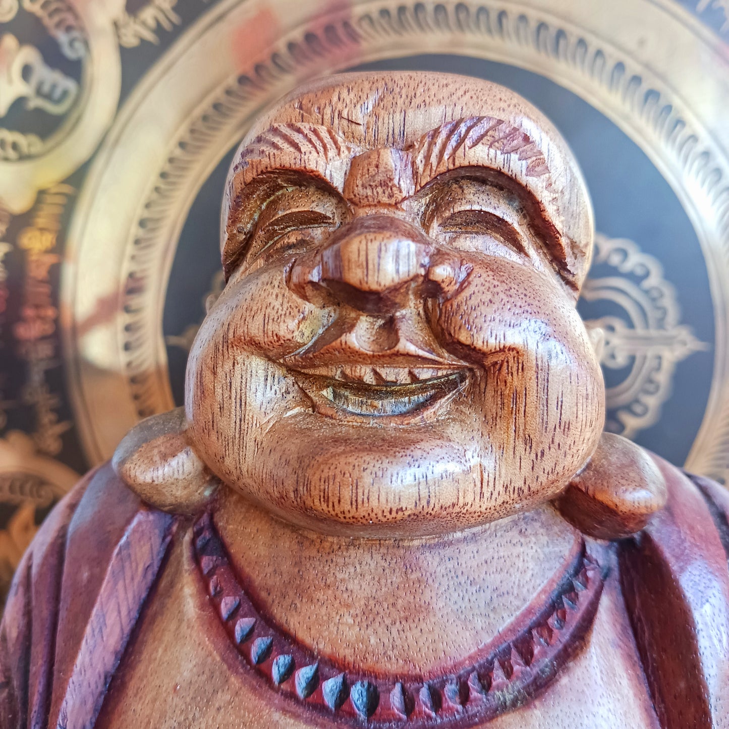 This charming Hand Carved Laughing Buddha is seated in a relaxed pose with a broad, joyful grin and rounded belly, beautifully carved from warm two-tone wood. The natural wood grain is enhanced with a protective varnish, highlighting the intricate details of his robes, prayer beads and expressive face.