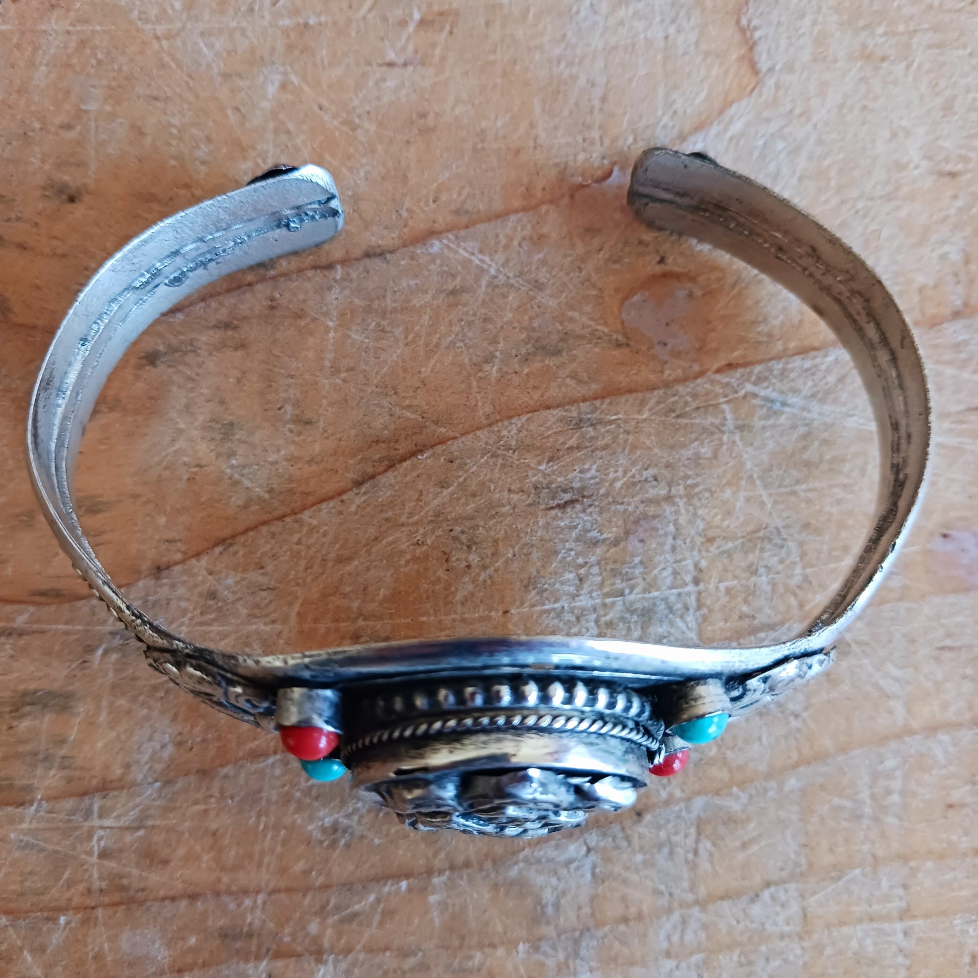 Embrace timeless elegance with this Endless Knot Tibetan Charm Bangle. Crafted from high-quality white metal and adorned with vibrant turquoise and coral semi-precious stones, this adjustable bangle showcases the sacred Endless Knot symbol on the front.