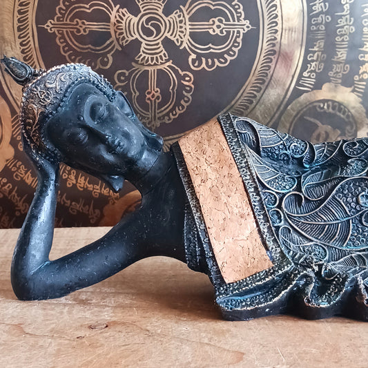 The statue features the Buddha in a graceful reclining pose, symbolizing his entry into nirvana. His left arm rests peacefully by his side, while his right hand cradles his head in a gesture of repose. The robe is intricately adorned with bodhi leaf motifs—sacred symbols of enlightenment and spiritual awakening.