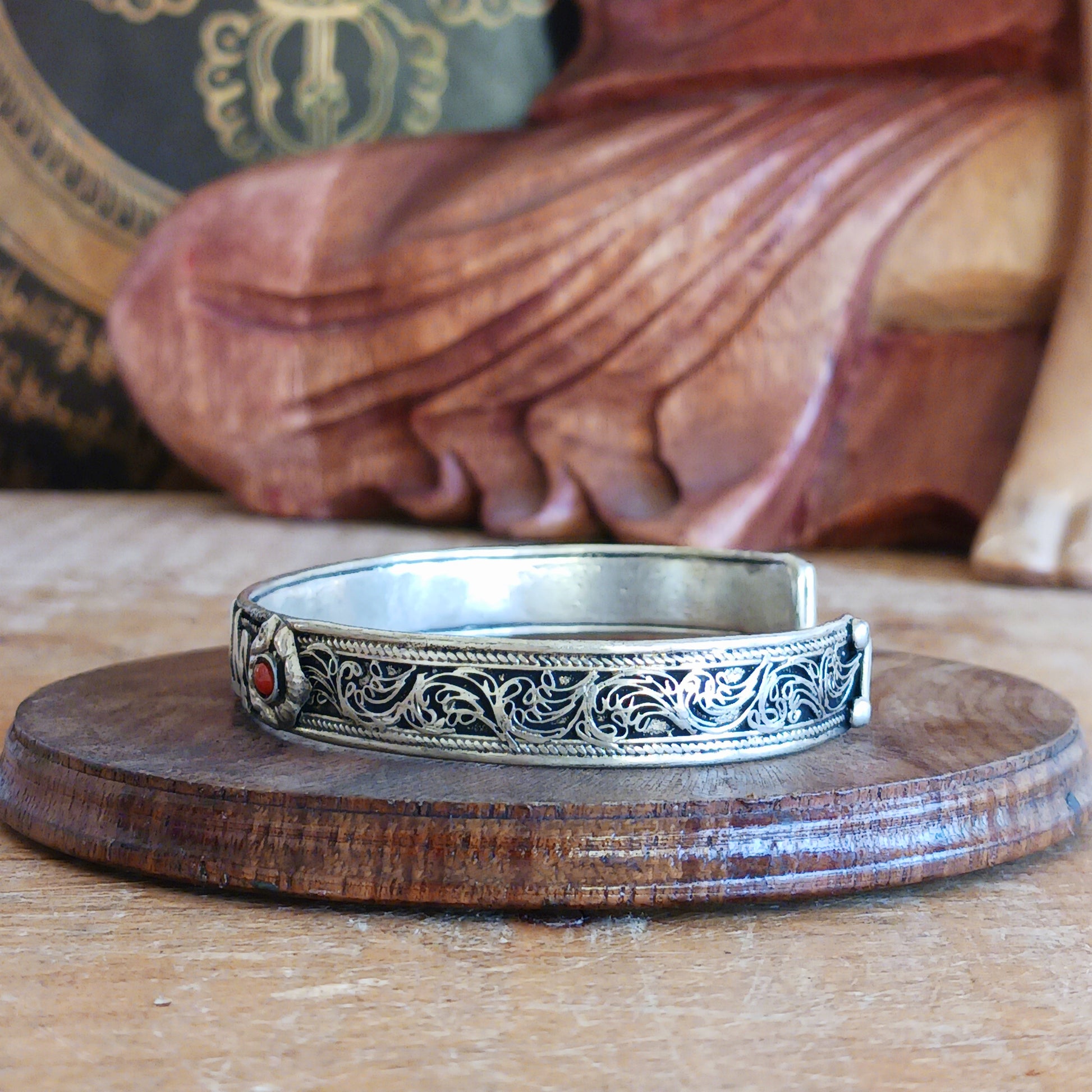 This Tibetan adjustable mantra bangle is a timeless piece of spiritual jewellery, handcrafted by skilled artisans in Nepal. Made from traditional Tibetan White Metal, the bangle features two small coral stones and engraved script inspired by ancient Tibetan culture and symbolism.